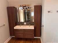 Front view of complete vanity setup showing double sink, two tall cabinets, mirror, backsplash, faucets