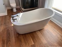 Side angle of white freestanding bathtub with chrome faucet, showing profile and flooring for size context