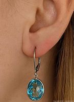 Earring worn in ear to show size and drop; single oval blue stone visible