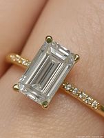 Emerald-cut lab diamond center stone on gold band with accent diamonds