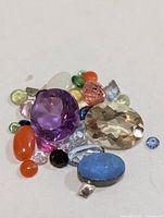 Group of assorted loose gemstones of various colours and cuts displayed on white background