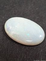 Oval white opal cabochon on dark background showing play-of-color