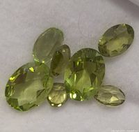 Seven oval faceted peridot gemstones on white background