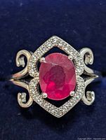 Top view showing oval ruby, halo of clear stones, scroll shoulders