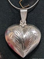 Heart-shaped silver pendant close-up showing etched leaf design