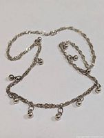 Full view of silver rope chain necklace with dangling ball accents laid flat