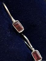 close-up of two silver earrings showing rectangular garnet stones set in bezels on navy background