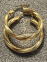 Pair of twisted gold hoop earrings on fabric background