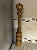 Full view of tall wooden pepper mill standing on countertop