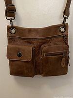 Front view of Roots brown leather crossbody bag showing pockets and strap