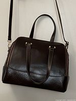 Front view of dark brown leather satchel showing structure, handles, and shoulder strap