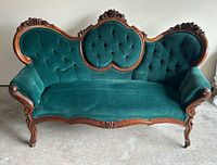 Full front view of carved wood Victorian settee showing green velvet upholstery and overall design