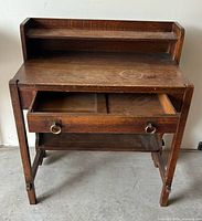 Front view of oak mission desk showing shelf, writing surface, open drawer, stretcher shelf