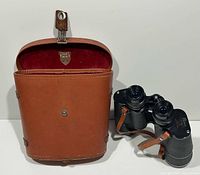 Binoculars beside open brown leather case, velvet interior visible