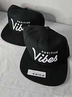 Two black Positive Vibes snapback hats, front view showing embroidery