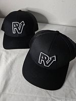 Two black RV logo trucker hats displayed on white surface