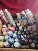 Open box showing numerous assorted acrylic paint bottles