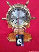Front view of brass ship’s wheel clock on oak base