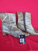 Side view of both boots showing metallic finish, decorative lacing, heel shape, lot tag 038 visible