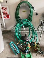 Overall lot showing two coils of hoses on wall and floor with attached watering wands, sprinklers and fittings