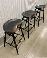 Three wood saddle-seat bar stools lined up side view