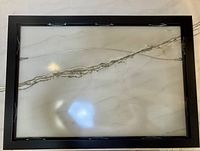 Back of black metal frame showing hanging wire and spring clips