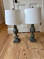 Front view of both matching sage green table lamps on wooden floor