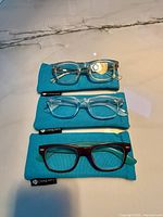 Three pairs Peepers glasses stacked on individual teal cases