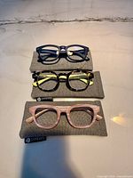 Three pairs of Peepers reading glasses on grey cases