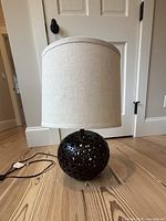 Front view of lamp showing spherical perforated base and linen shade