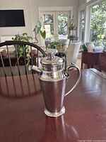Full view of silver-plated cocktail shaker standing on table