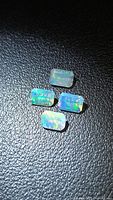 Four emerald-cut opals on dark surface, displaying color play