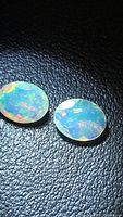 Pair of oval faceted opals on dark textured background showing color play