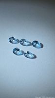 Five pear-cut blue topaz gemstones shown on neutral background