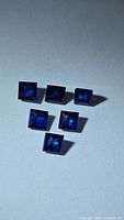 Six square deep blue sapphires arranged on light background