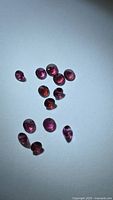 Group of 12 round faceted pinkish-purple garnets on white background