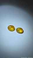 Pair of golden yellow oval cabochon sapphires on light background