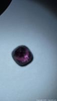 Blurry view of purple pink cushion-cut gemstone on white surface
