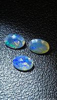 Three faceted oval opals on black textured surface showing blue and green fire