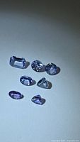 Seven faceted Tanzanite gemstones arranged on neutral background