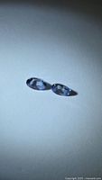 Two oval bluish-violet tanzanite gemstones on neutral background
