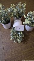 Four small artificial potted plants displayed on floor with lot card