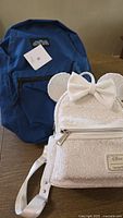 White Disney Loungefly mini backpack and plain blue backpack on table