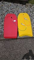 Red Morey and yellow Mano Shok boogie boards lying side by side showing tops, leashes attached