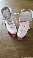 Top view of pair of white children’s roller skates with pink wheels and size tag