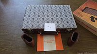 Closed cloth patterned case, two leatherette dice cups, rules booklet, partial view of cardboard sleeve
