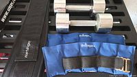 Weightlifting belt, ankle weights pair, two chrome dumbbells on surface