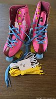 Front view of pink Hype roller skates with blue laces, yellow wheels, extra yellow and white laces displayed