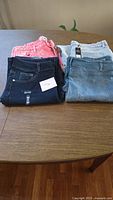 Four stacked pairs of jeans in pink, dark blue, medium blue with tag, and light blue on tabletop