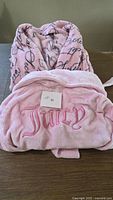 Two pink robes stacked: top Victoria’s Secret script robe, bottom Juicy Couture robe showing embroidered "Juicy"